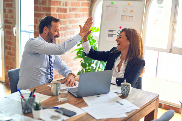 A happy man and woman in an office doing hi five. They seem to be celebrating something.