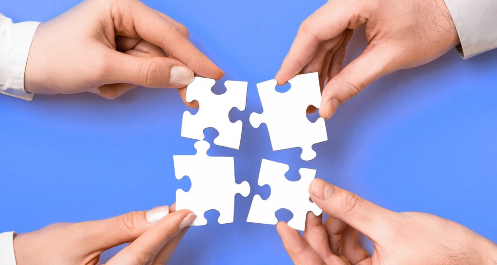 Four hands holding puzzle pieces